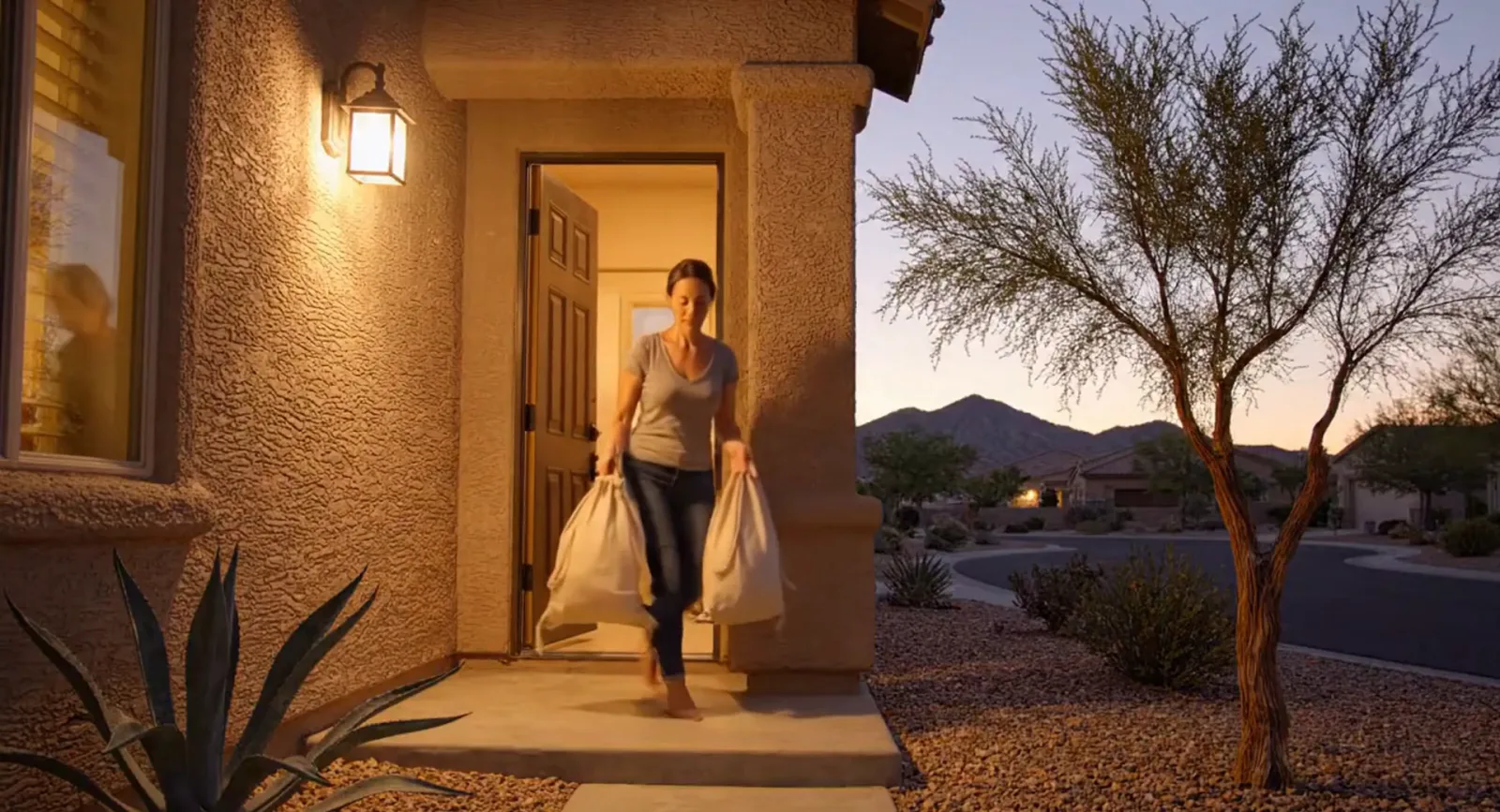 An Everlast driver carrying laundry bags out of a Henderson doorway at dusk